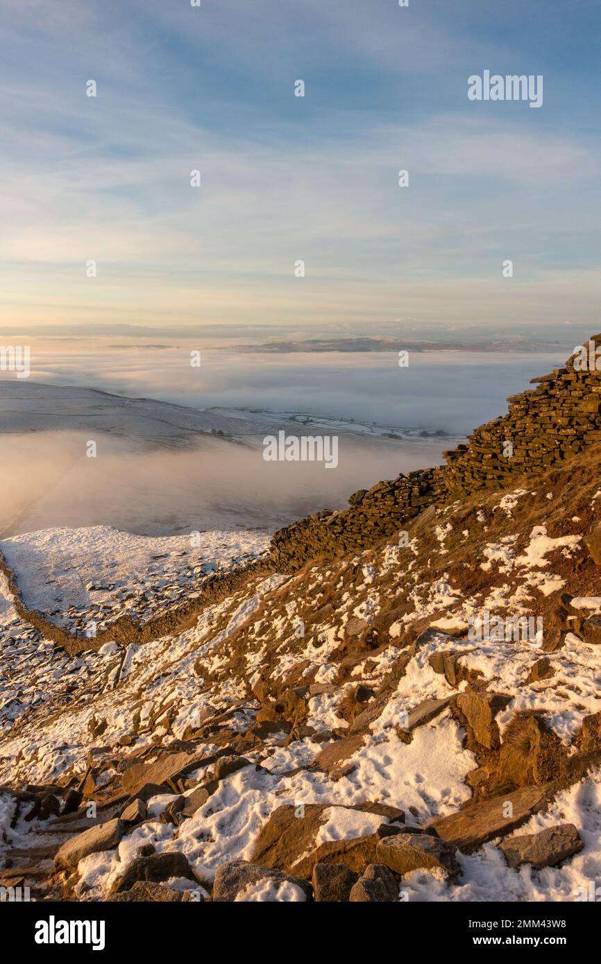 Looking down the stone wall towards from the final path to the summit of Pen-y-ghent mountain at sunrise with mist and snow in the Yorkshire Dales Nat Stock Photo