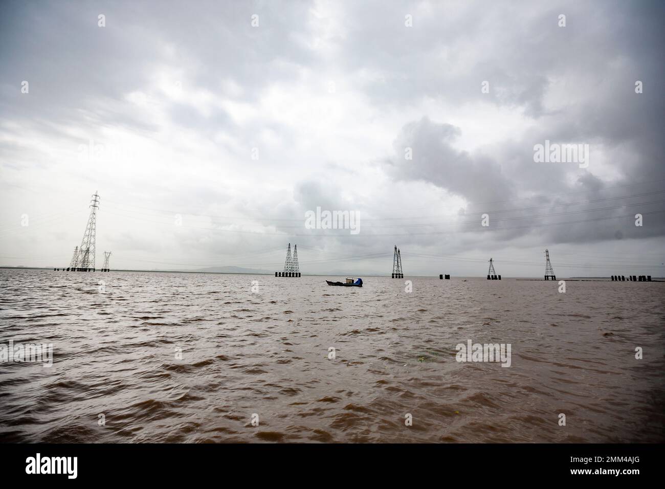 Brown sea water with boats and high Voltage electric lines Stock Photo