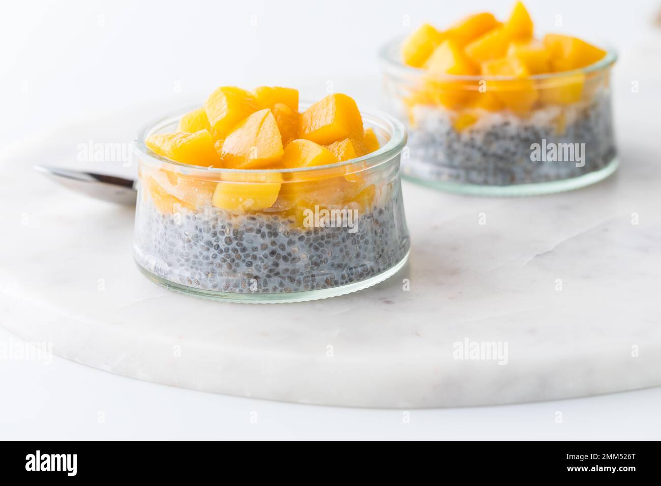 Two chia pudding snacks topped with chopped cubes of mango, on a marble slab. Stock Photo