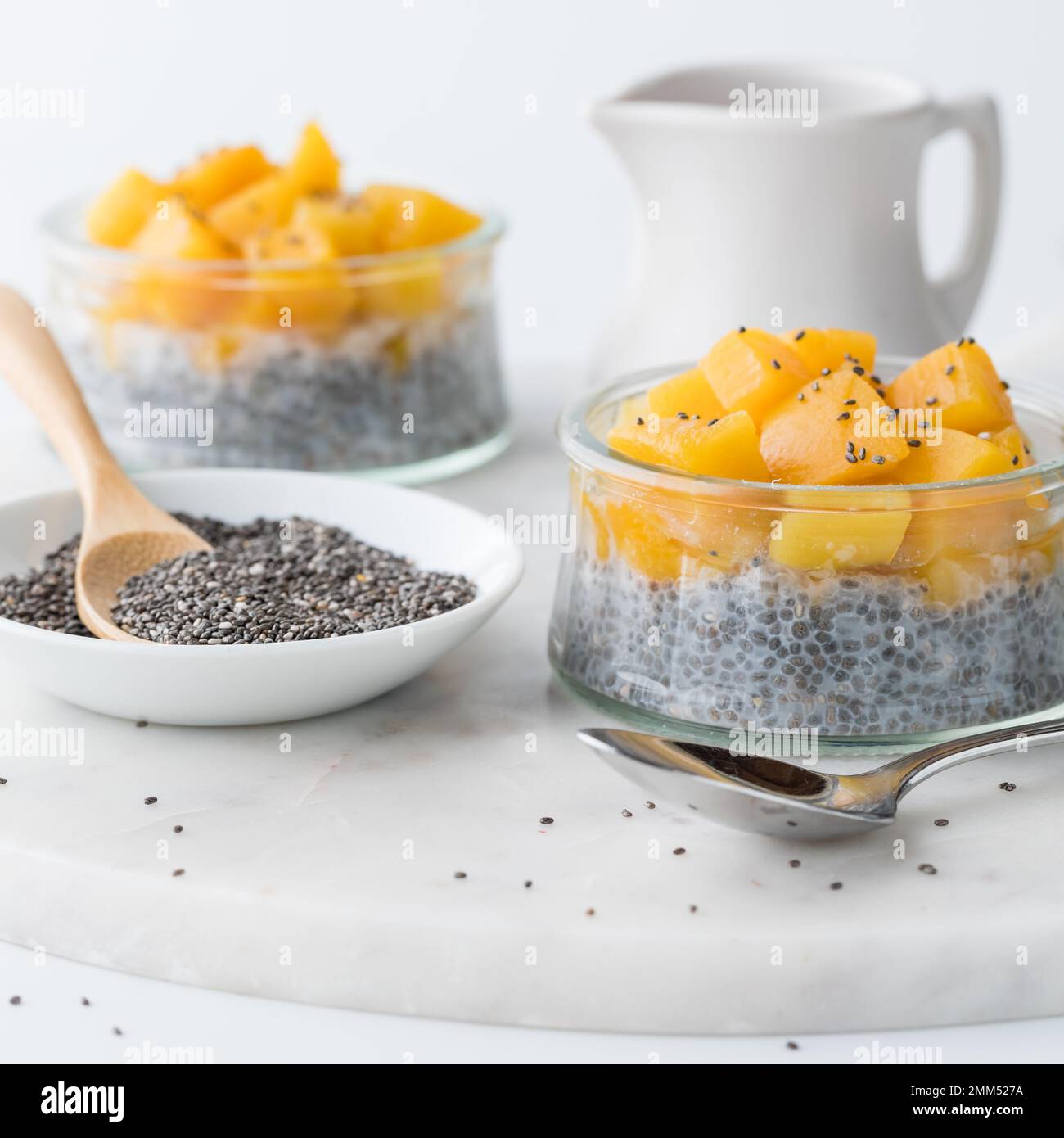 Two chia pudding parfaits topped with diced mangos and a bowl of chia seeds. Stock Photo