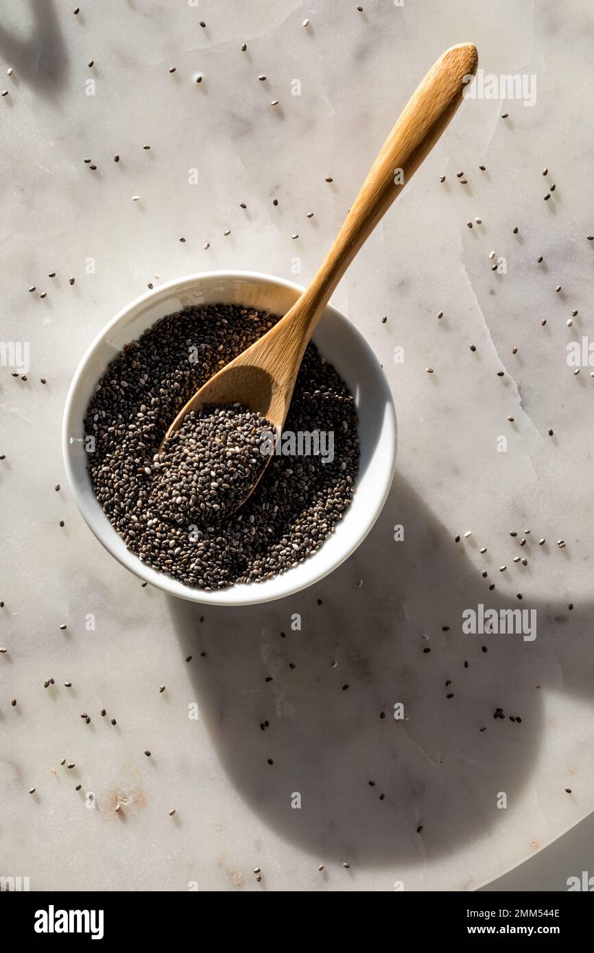 Top down view of a bowl of chia seeds on a marble slab in bright sunlight. Stock Photo