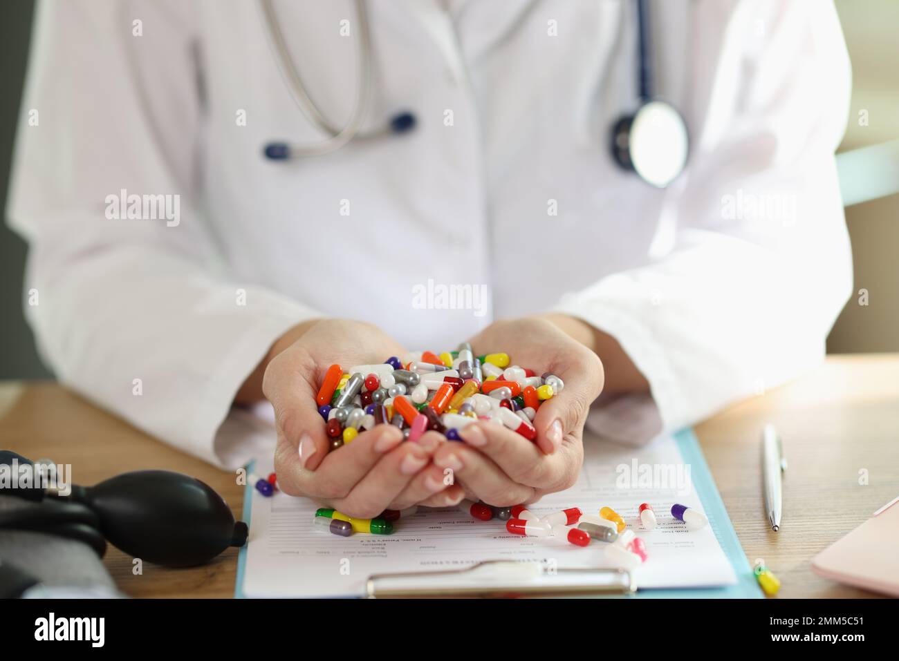 Doctor with stethoscope holds bunch of multi-colored pills in her hands close up. Stock Photo