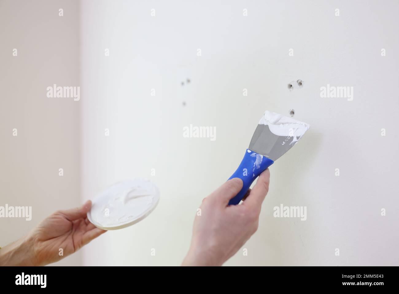 Builder or repairman with putty knife plastering white wall close up. Stock Photo