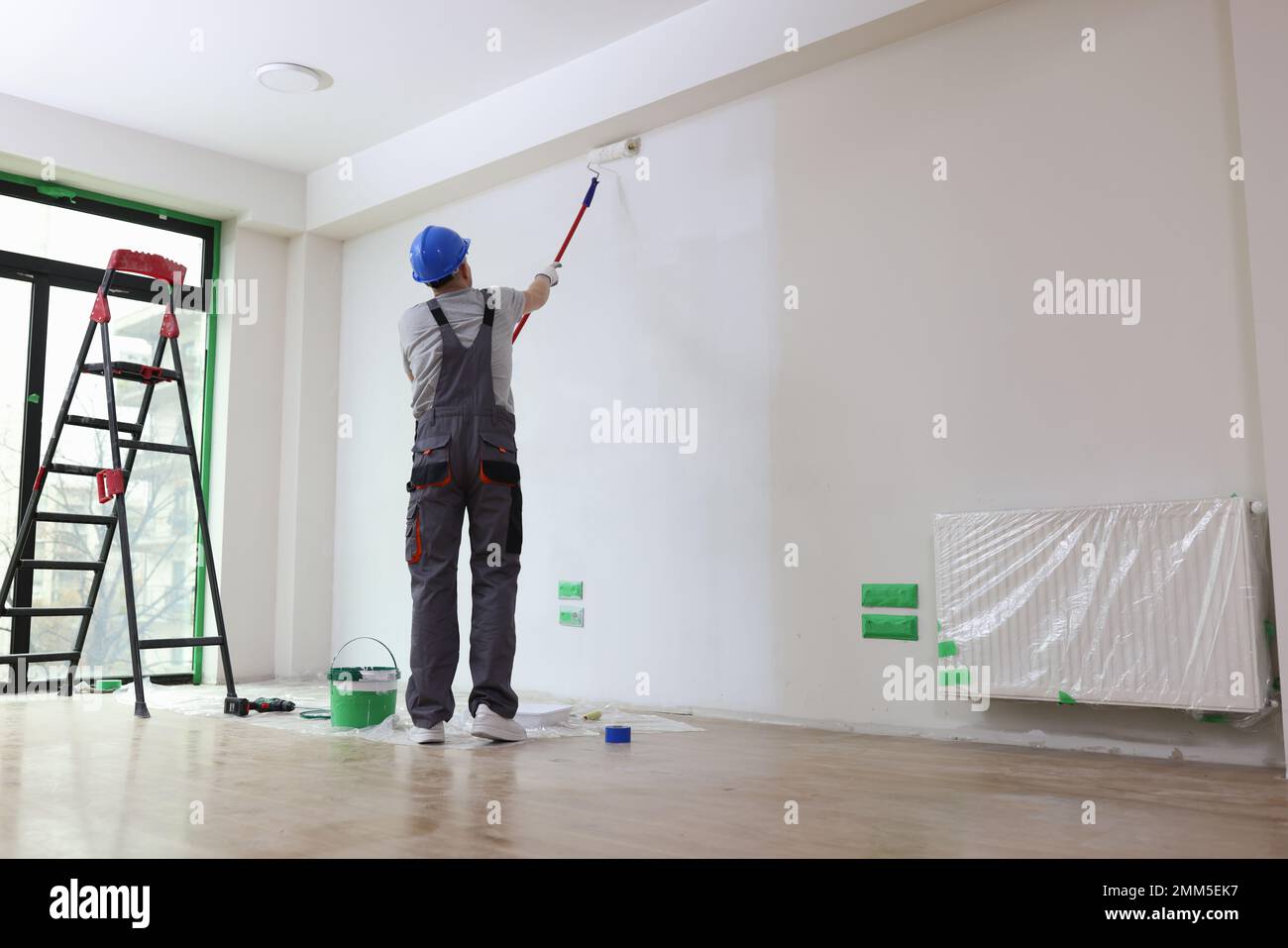 Professional painter paints office wall with roller brush. Stock Photo