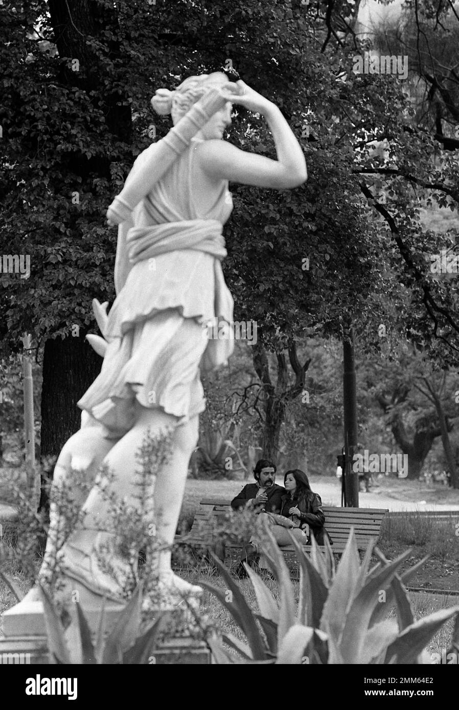 Couple seated on bench in Barrancas de Belgrano with statue in the foreground, Buenos Aires, Argentina Stock Photo
