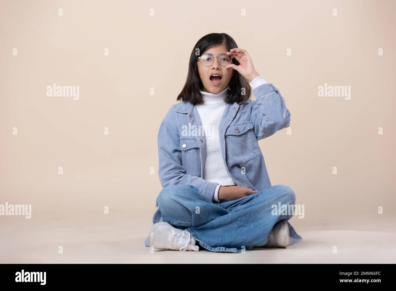 Mexican girl sitting on the floor wearing glasses surprised face Stock Photo