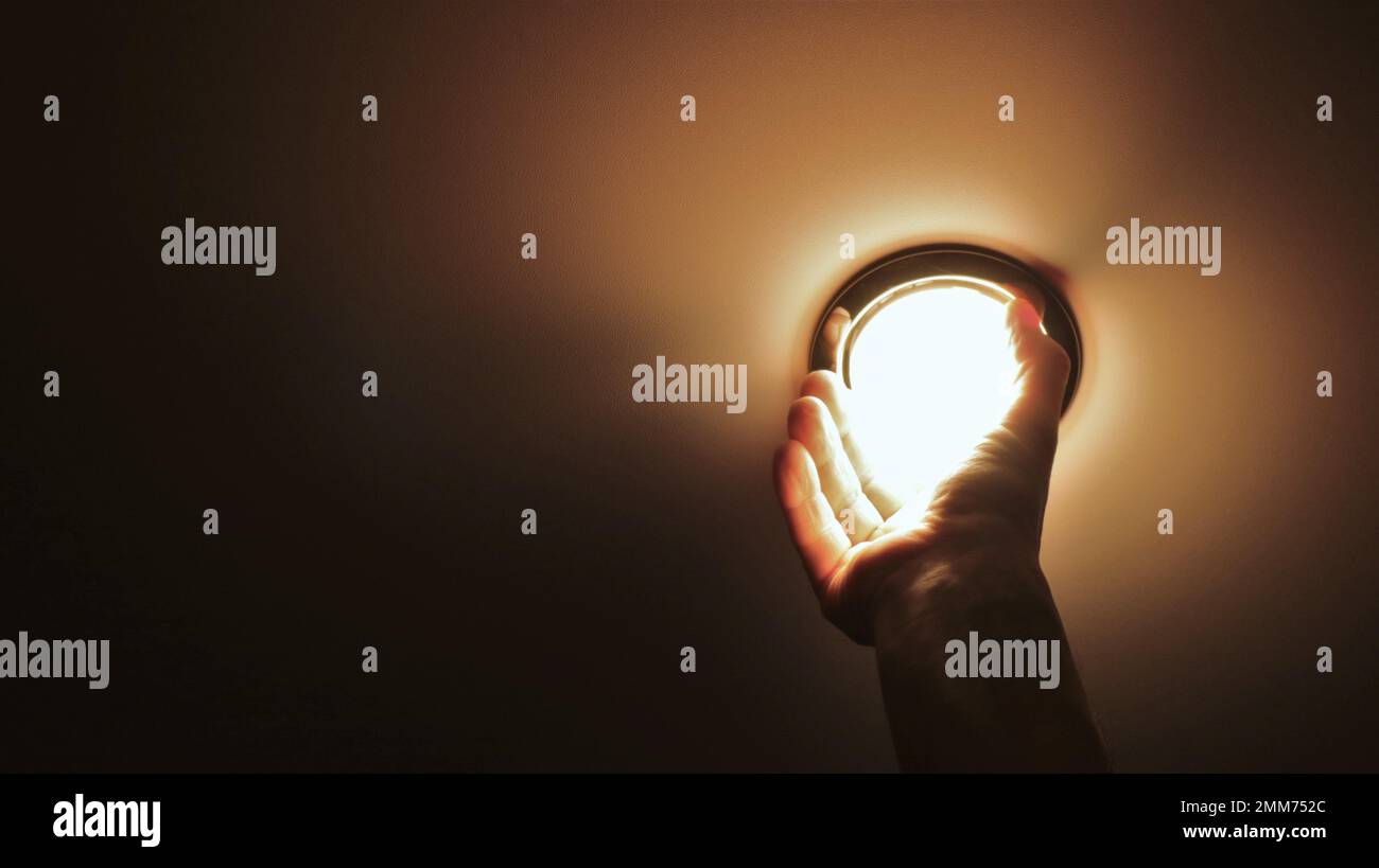 a man's hand screwing a round bright lamp into a flat ceiling, a light ...
