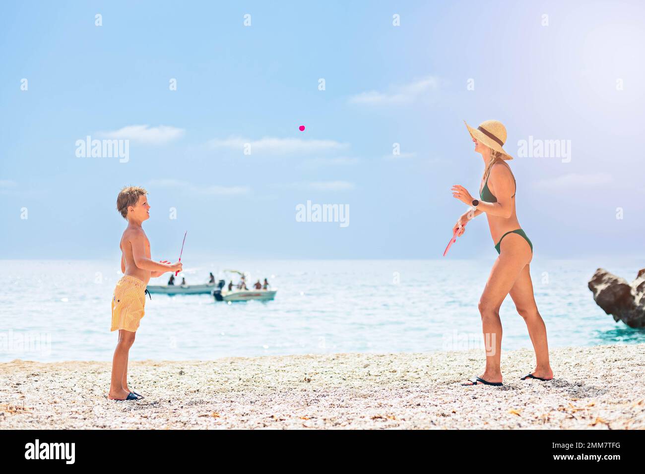 Mom in a green bathing suit and straw sun hat plays with her son on the beach Stock Photo
