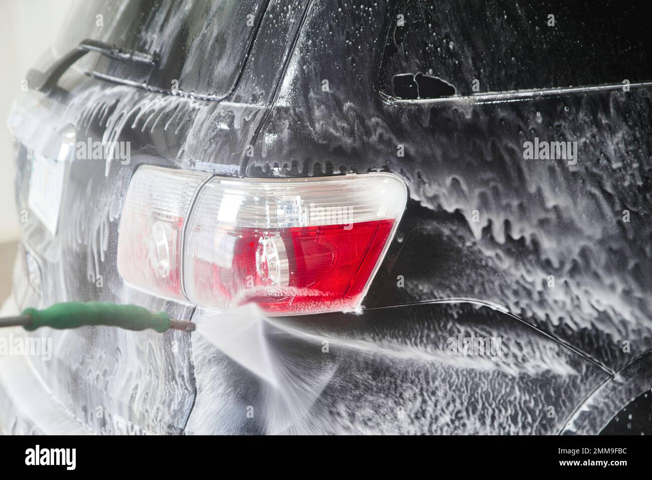 Soapy water spraying out from a wand washing the red tail light of a car Stock Photo
