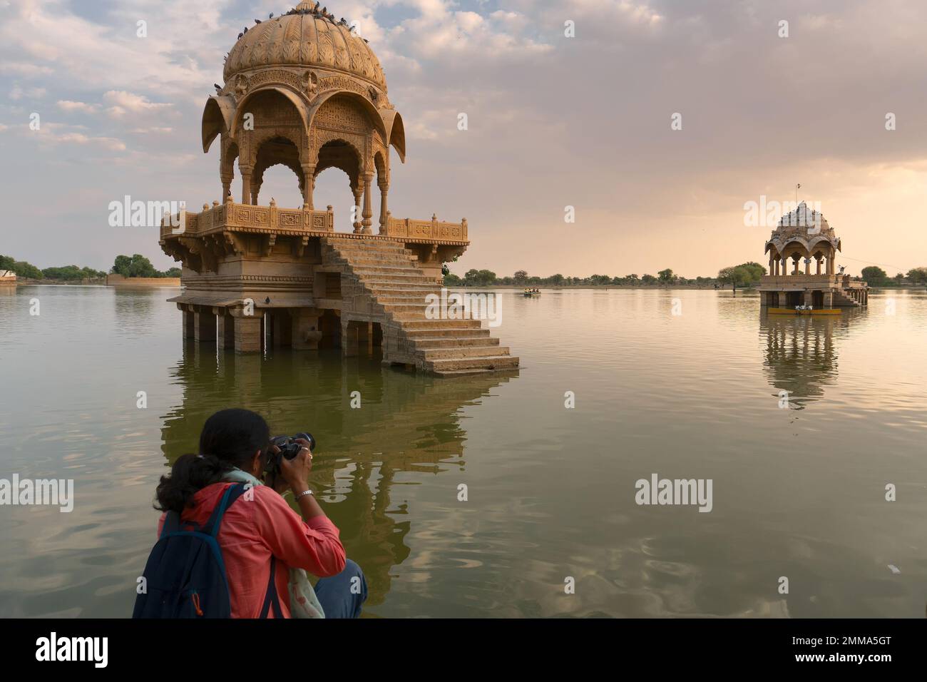 Indian female traveller, woman photographer taking picture of Chhatris and shrines with reflection of them on the water of Gadisar lake; Jaisalmer. Stock Photo