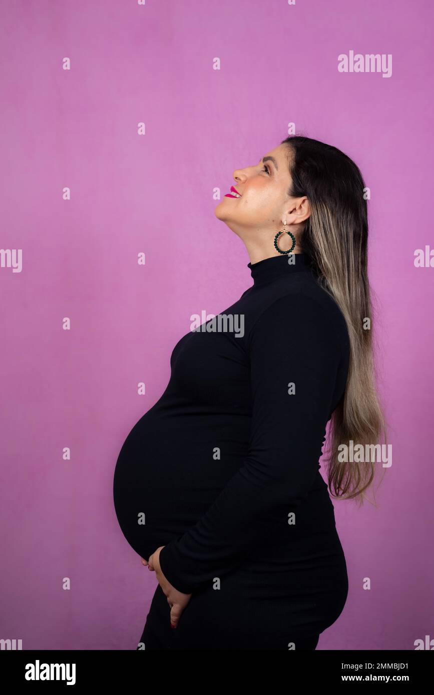 Pregnant woman in profile holding the barria with her hands. Isolated against pink background. Stock Photo