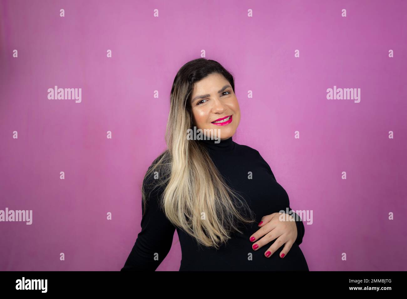 Pregnant woman holding barria with her hands. Isolated against pink background. Stock Photo