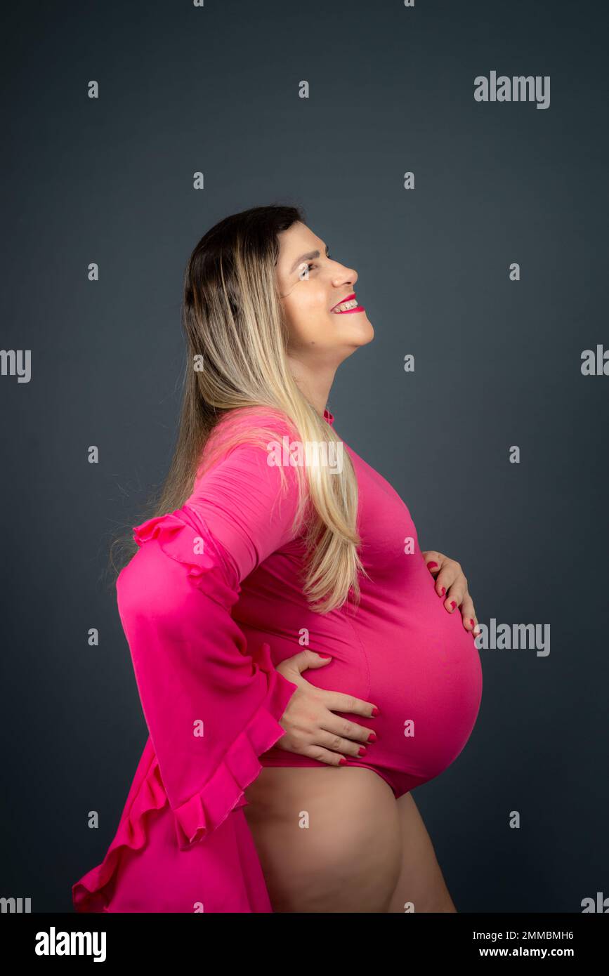 Pregnant woman in profile with hands on belly wearing pink outfit. Isolated against gray background. Stock Photo