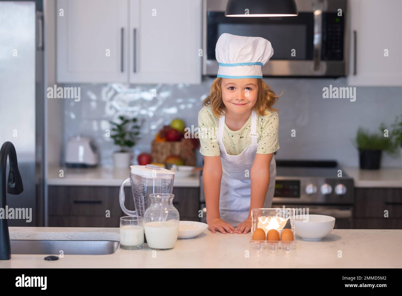 Kid chef cook wearing cooker uniform and chef hat preparing food on kitchen. Cooking, culinary and kids food concept. Stock Photo