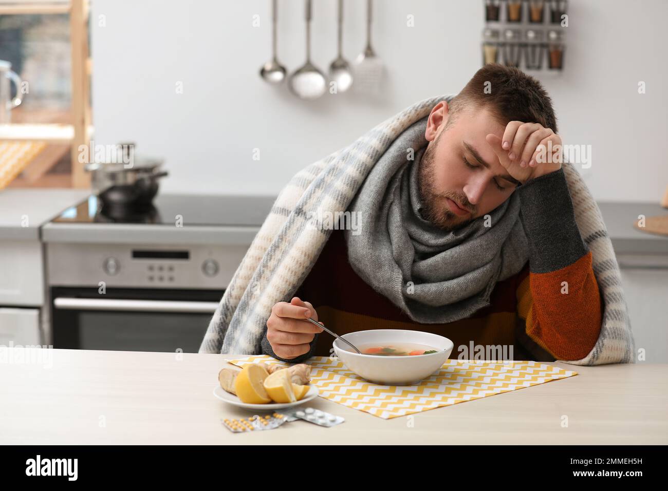 Sick young man eating tasty soup to cure flu at table in kitchen Stock