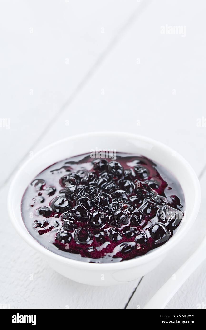 Fresh homemade jam made of Patagonian Calafate berries (lat. Berberis heterophylla), served in white bowl, photographed on white wood with copy space Stock Photo