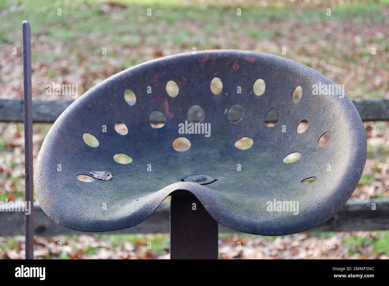 Vintage tractor seat with lever, shown with fence in background (along