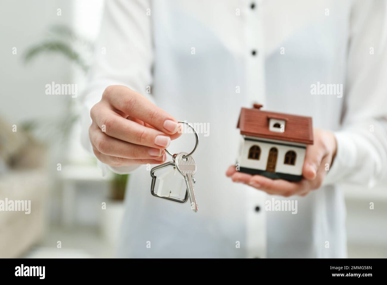 Real estate agent holding house model and key indoors, closeup Stock ...