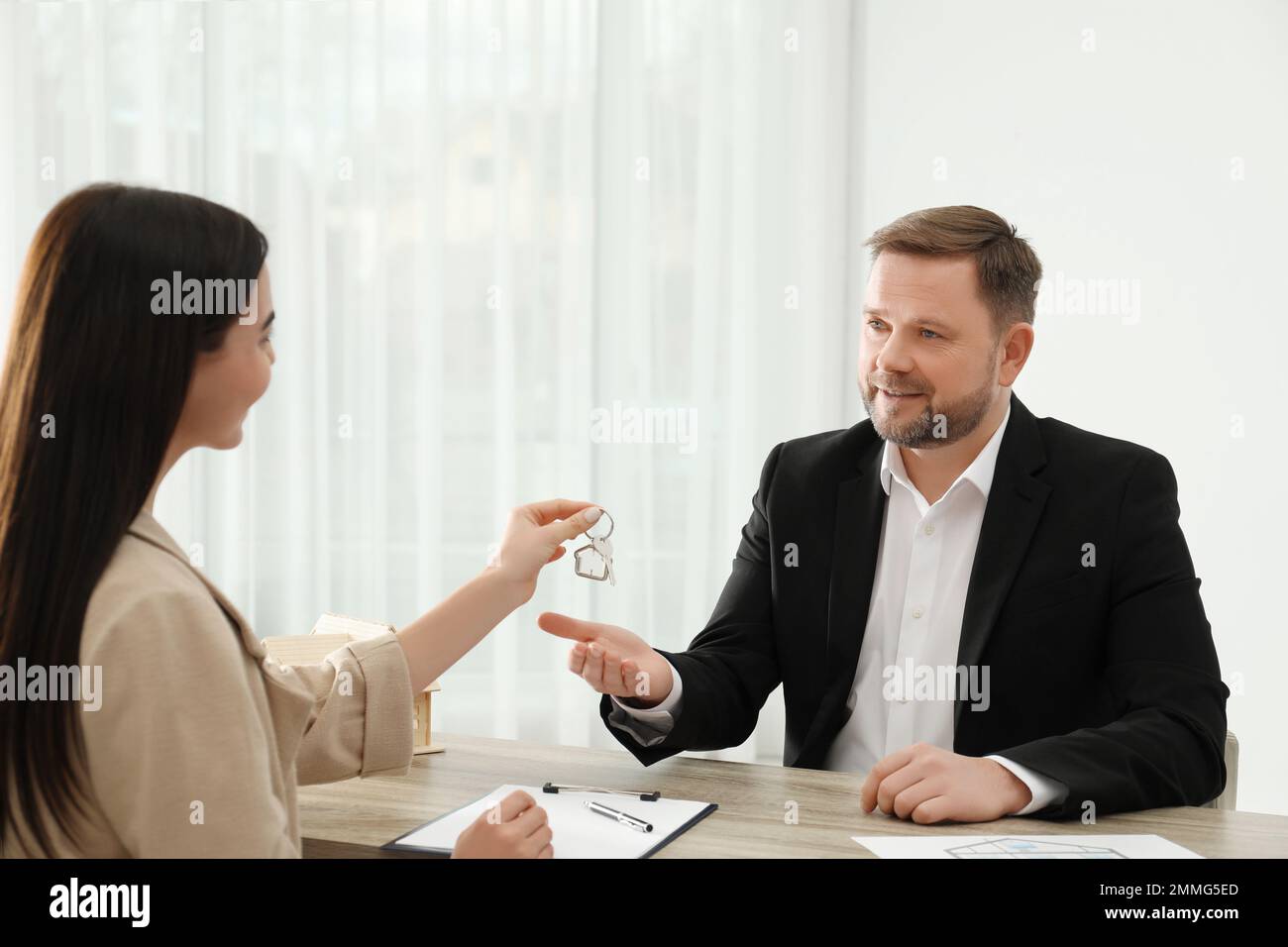 Real estate agent giving key to client at table in office Stock Photo ...