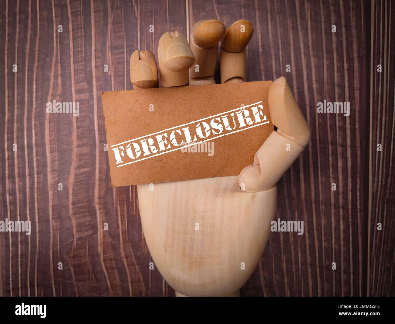 Wooden hand holding card board with the word FORECLOSURE on a wooden background. Stock Photo