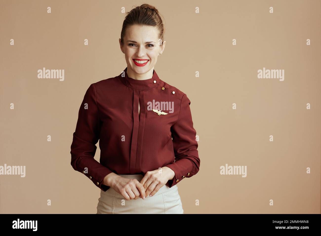 Portrait of smiling elegant female air hostess on beige background. Stock Photo