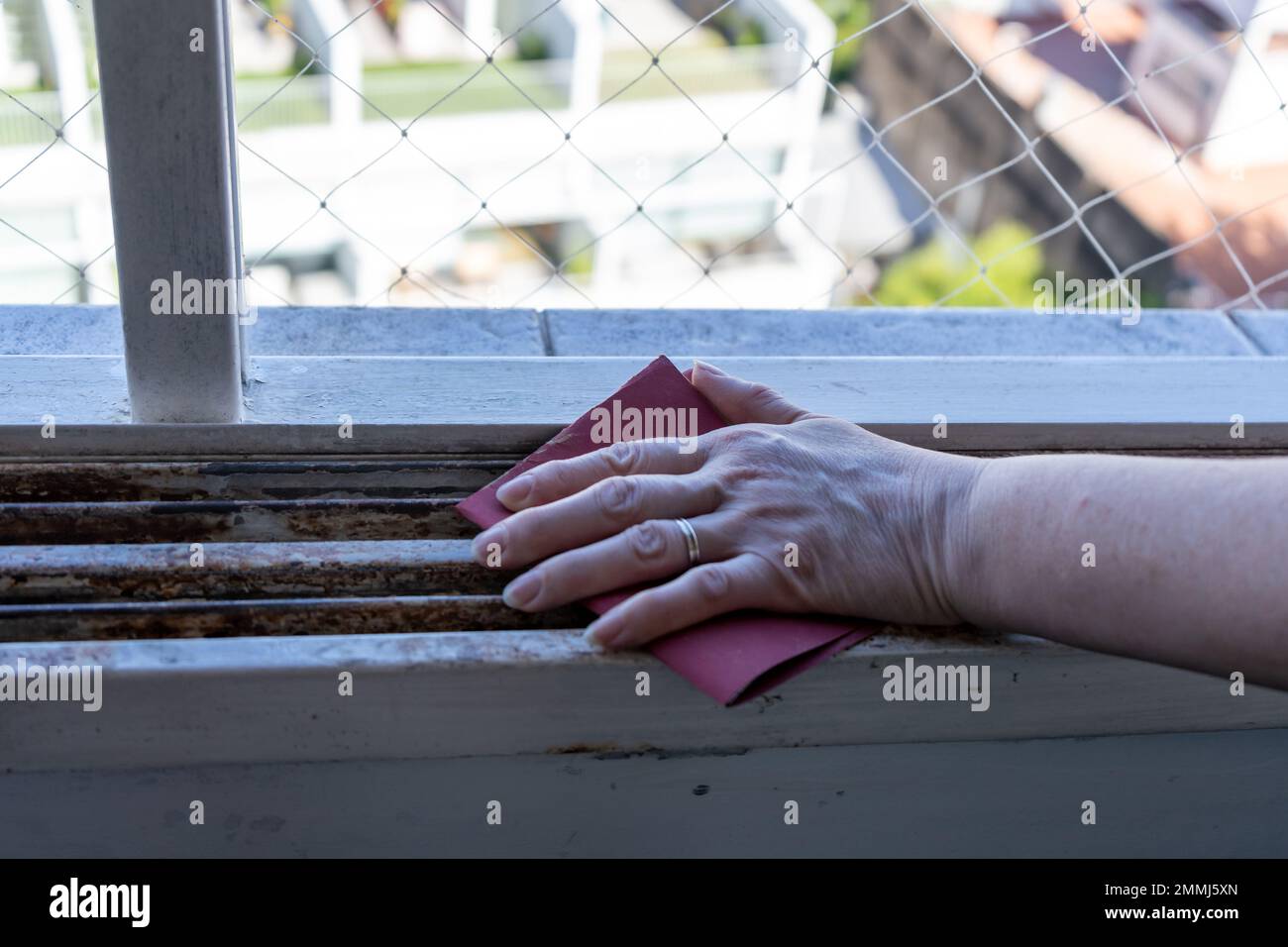 Hands of a woman with a sandpaper sanding a window frame before