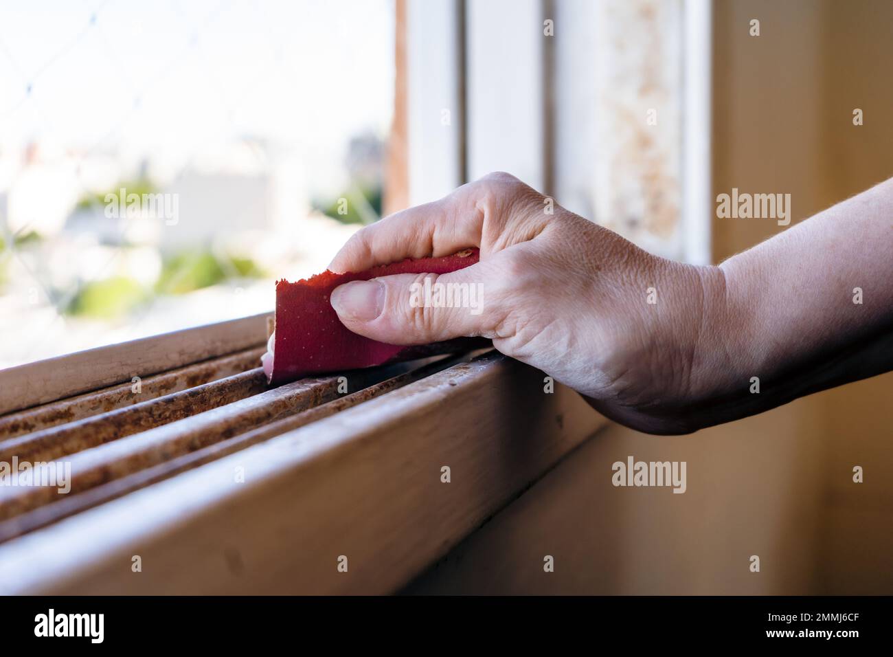 Normal view of a woman's hands with a sandpaper sanding an old window