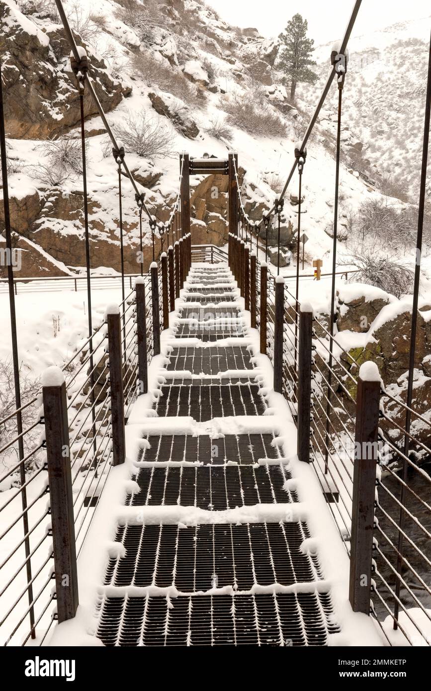 Snow-covered suspension bridge on Welch Ditch Trail in Clear Creek Canyon. Part of the Peaks to Plains Trail - near Golden, Colorado, USA Stock Photo
