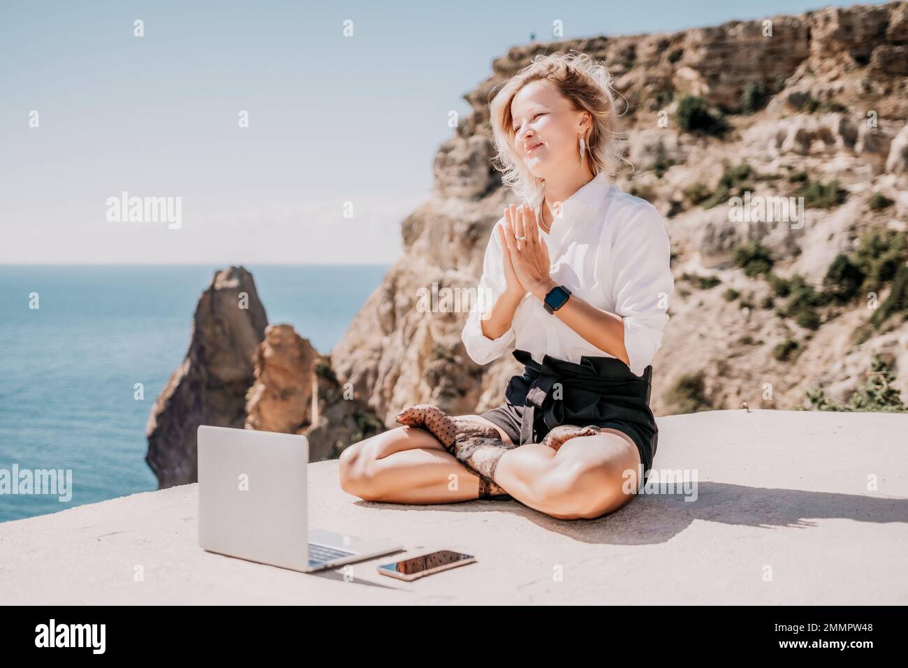 Woman sea laptop yoga. Business woman freelancer in yoga pose working over blue sea beach at laptop and meditates. Girl relieves stress from work Stock Photo