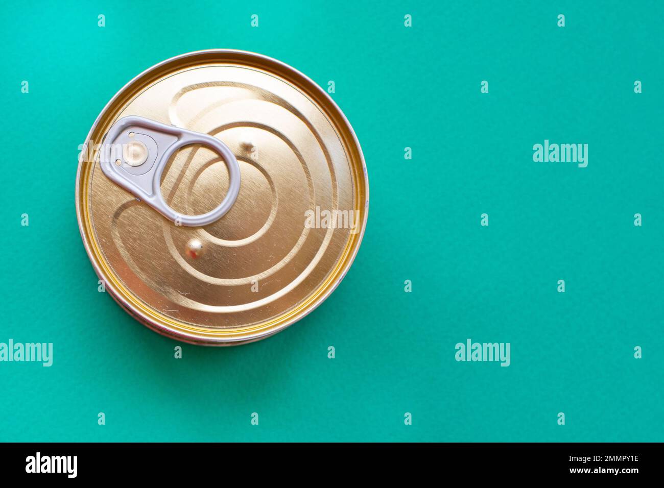 Easy-open metallic can lid on a green background. Top view of tin can with ring pull isolated on green background with copy space. Close-up Stock Photo