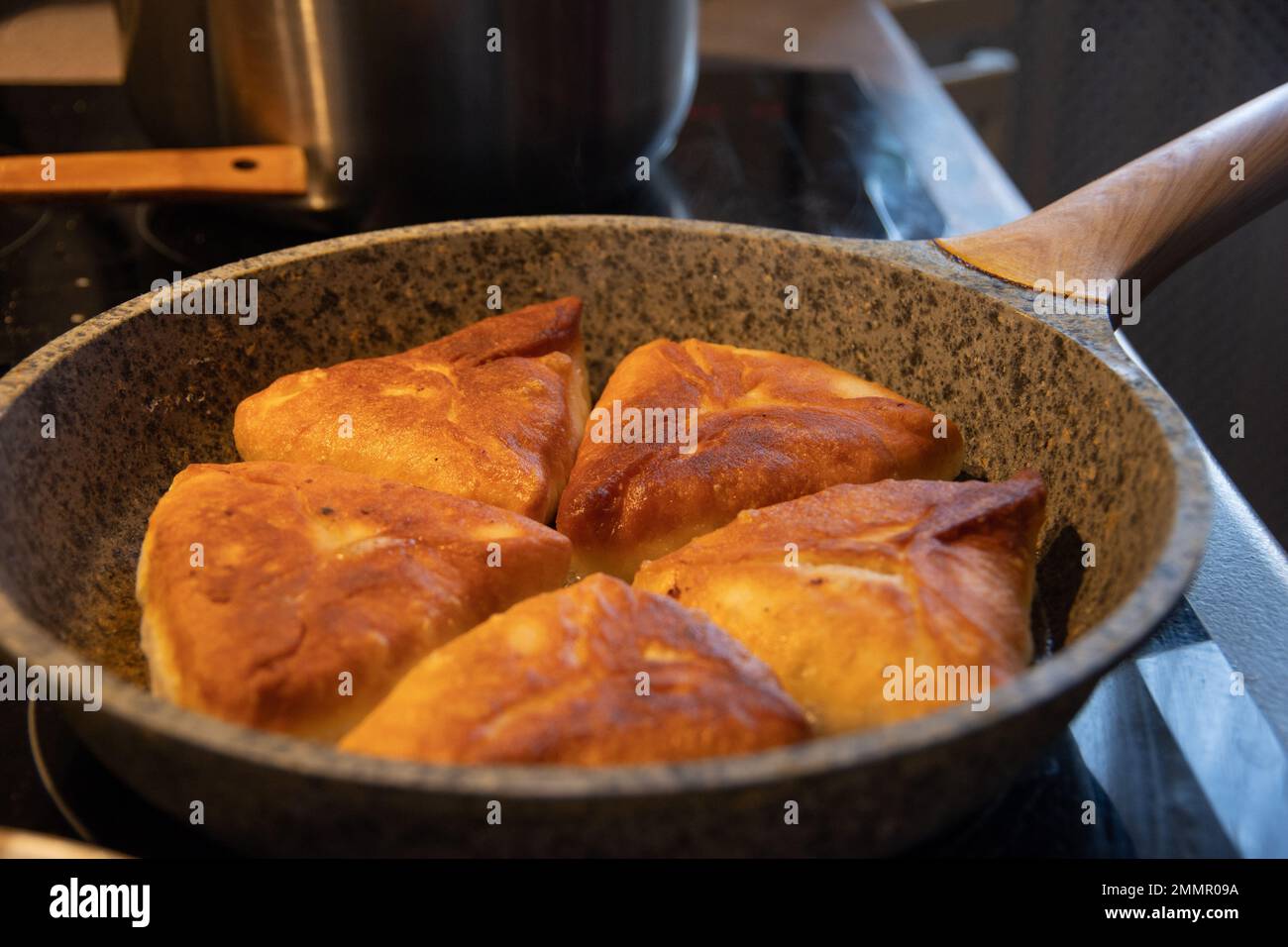 Fry delicious homemade lush pies with meat filling in hot vegetable oil. Pies are fried in a pan. Russian cuisine. Stock Photo
