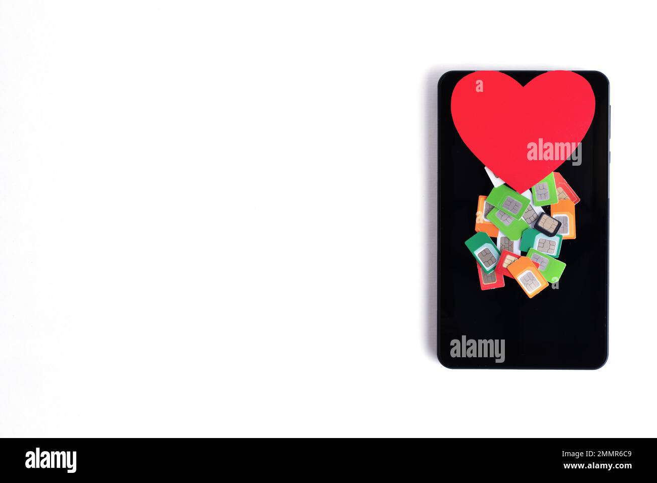 A pile of assorted used mobile SIM cards and a red paper heart on a cell phone on a white background, copy space. Cellular communication concept Stock Photo