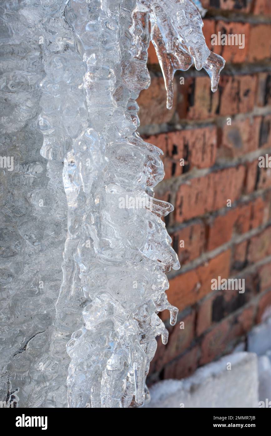 Very beautiful transparent icicles and ice hang from the drain pipe. Spring melting snow. Icicles falling danger concept Stock Photo