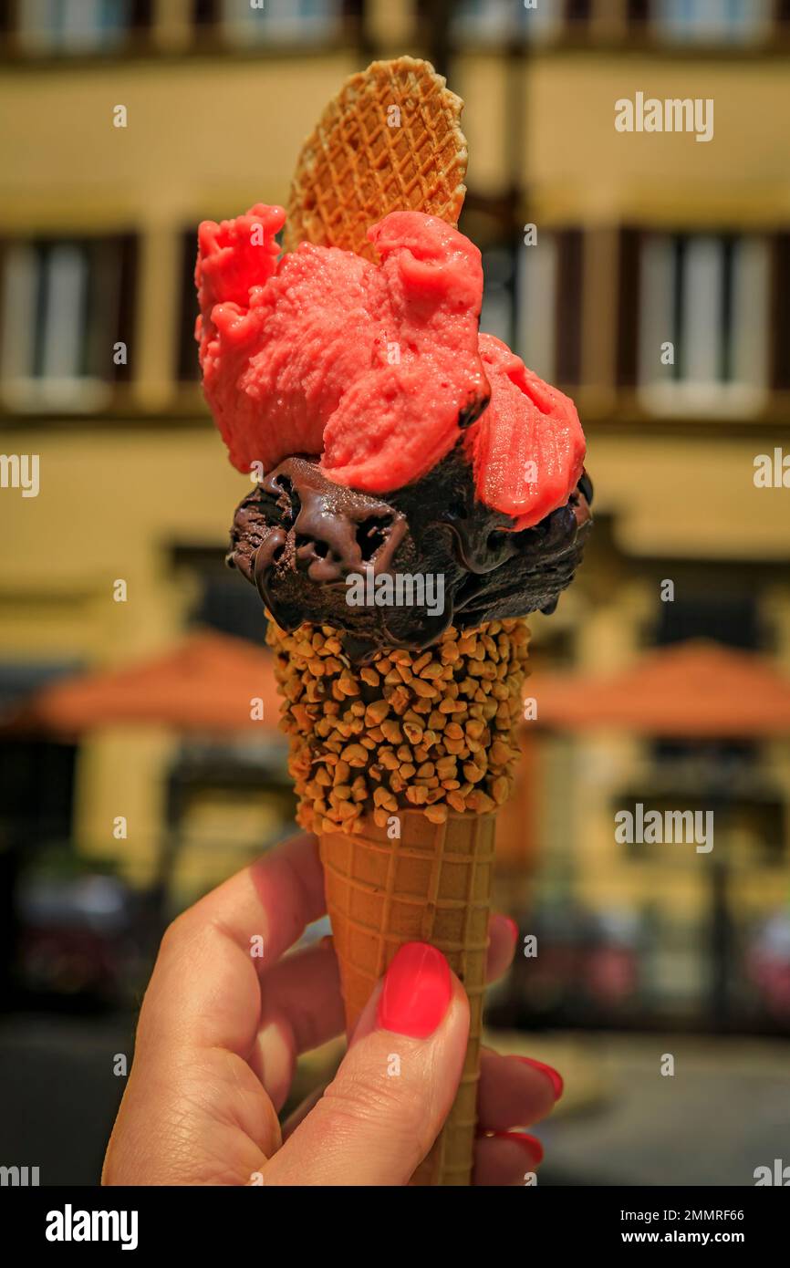 Hand holding an artisanal chocolate and raspberry gelato, a view of blurred houses and lights on a walking street in Centro Storico, Florence, Italy Stock Photo