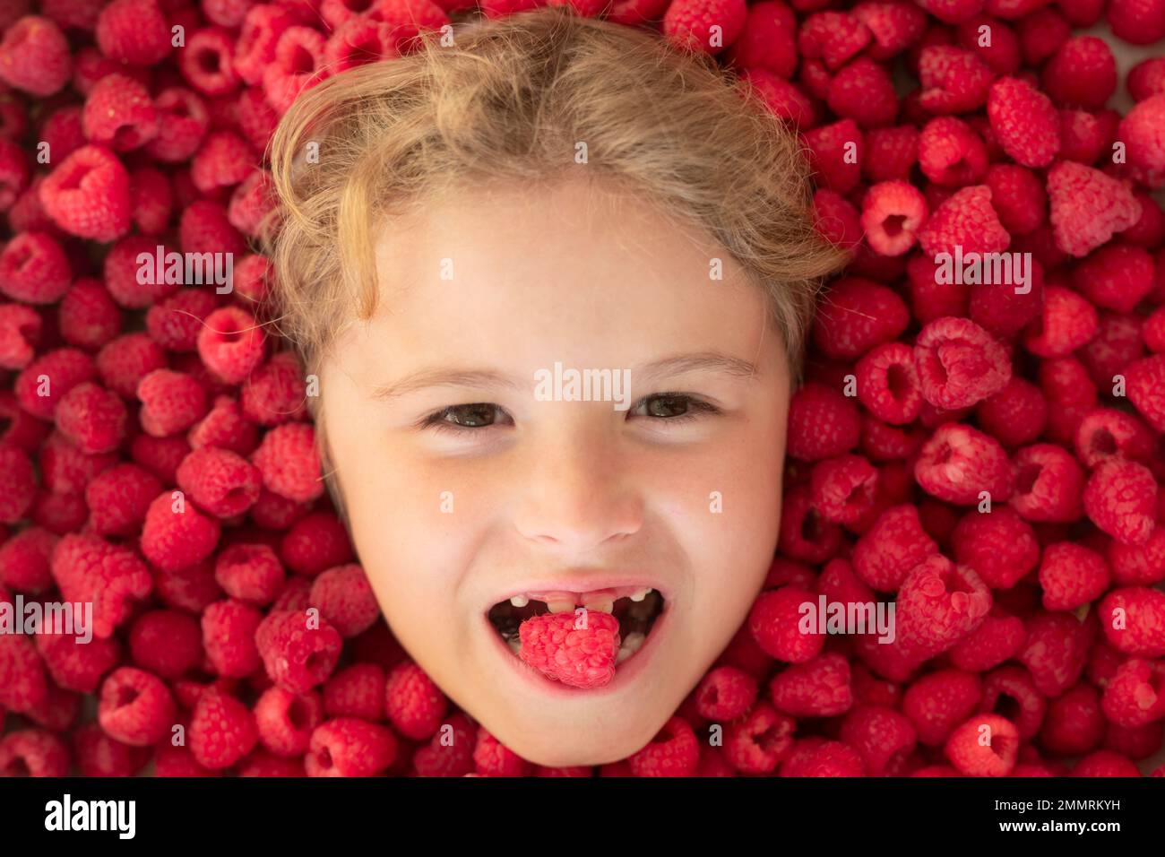 Raspberry in kids mouth. Kids face in raspberries fruits, healthy kids