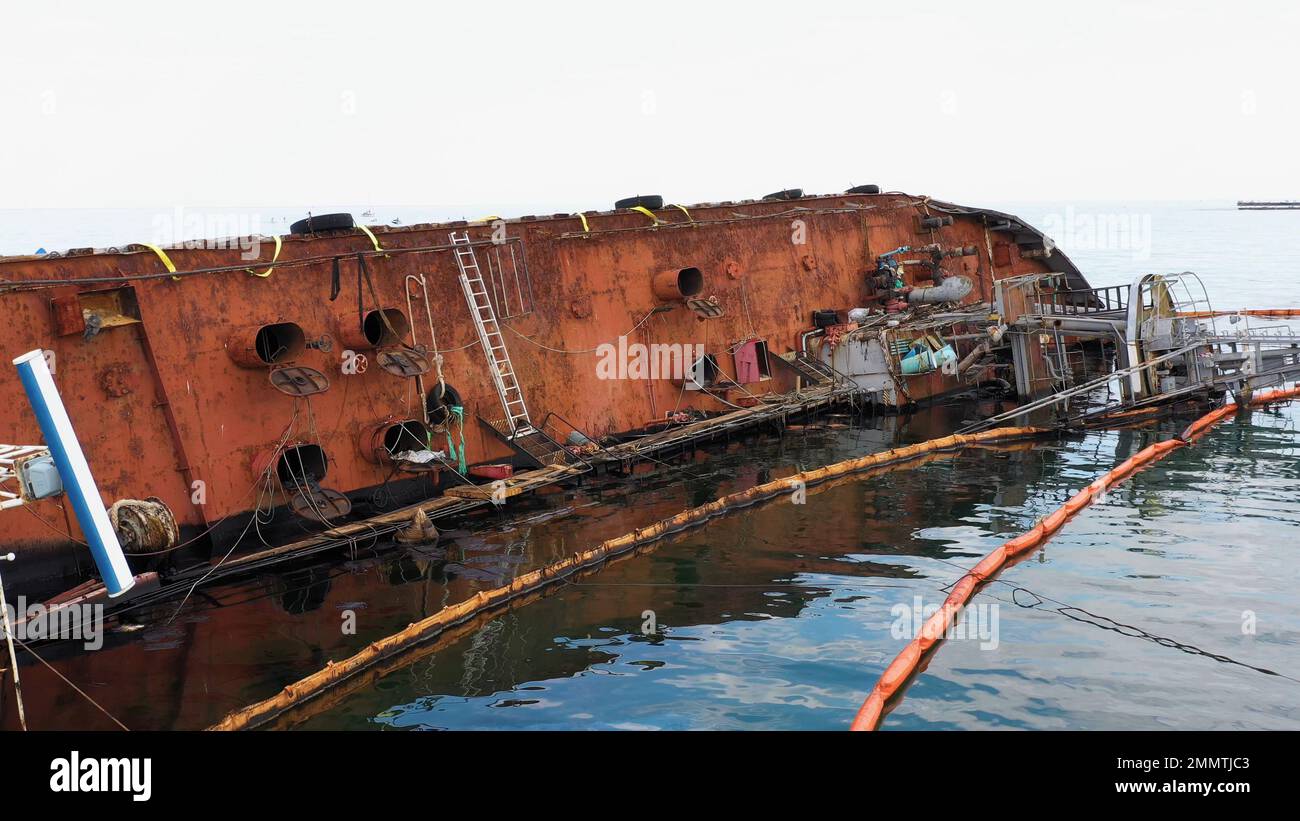 Old rusty overturned oil tanker lying on its edge in the shallow water. Sunken drowned ship after the wreck. Stock Photo