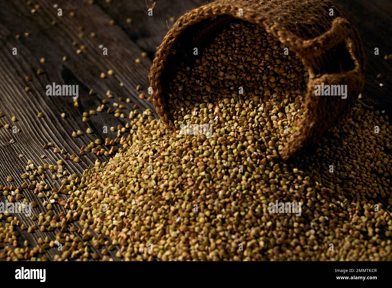 Green unprocessed buckwheat is scattered on the wooden table from an inverted jute bag Stock Photo