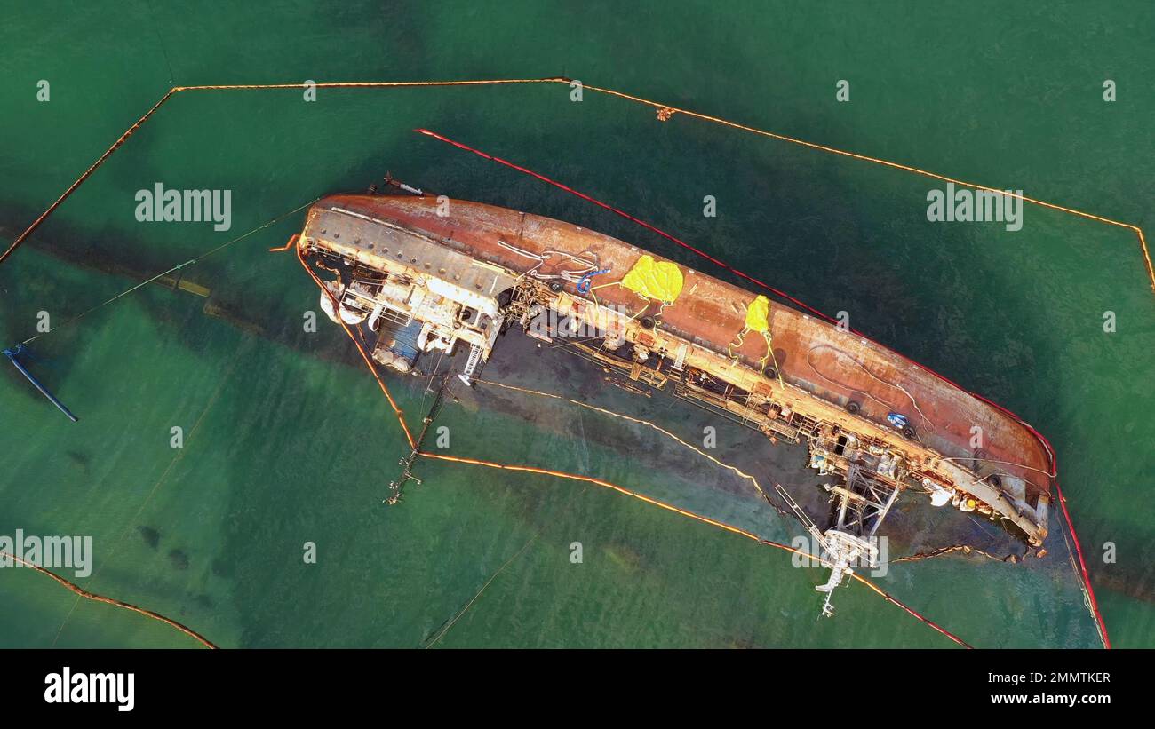 Aerial top view of overturned broken rusty oil tanker ship in the shallow water. Drowned ship after the wreck. Stock Photo