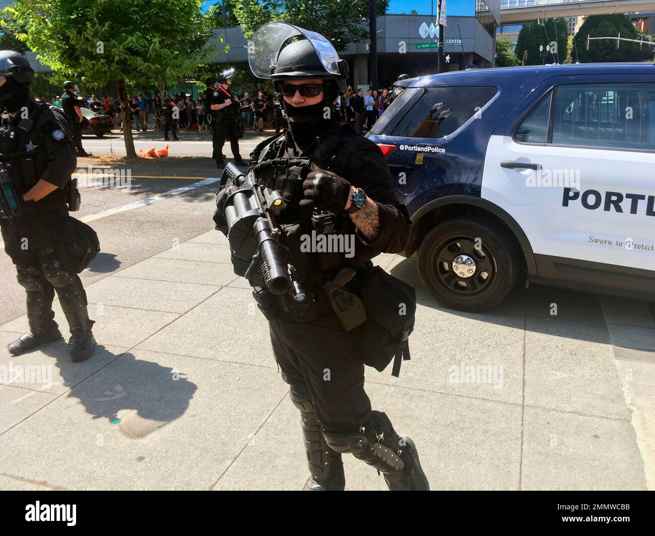 Portland police officers in riot gear stand by a police vehicle ...