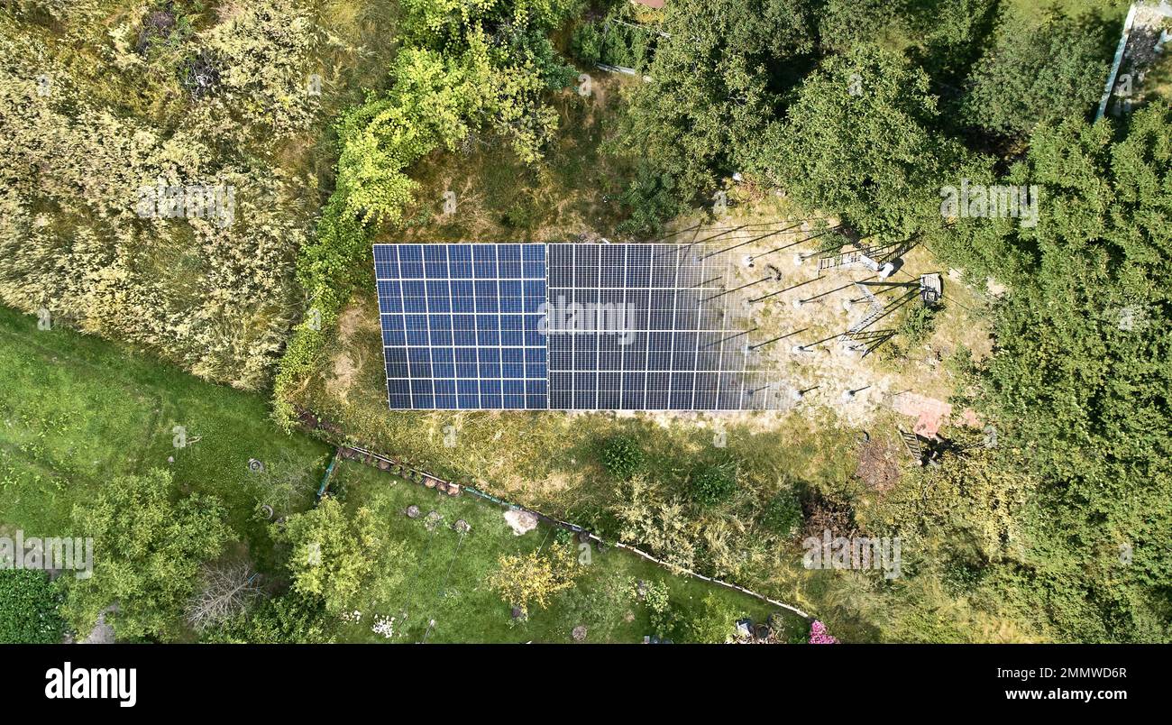 Aerial view of solar module fading away and shifting into metal supporting structure. Transition between solar panel and metal poles in grassy field with green trees. Before and after concept. Stock Photo