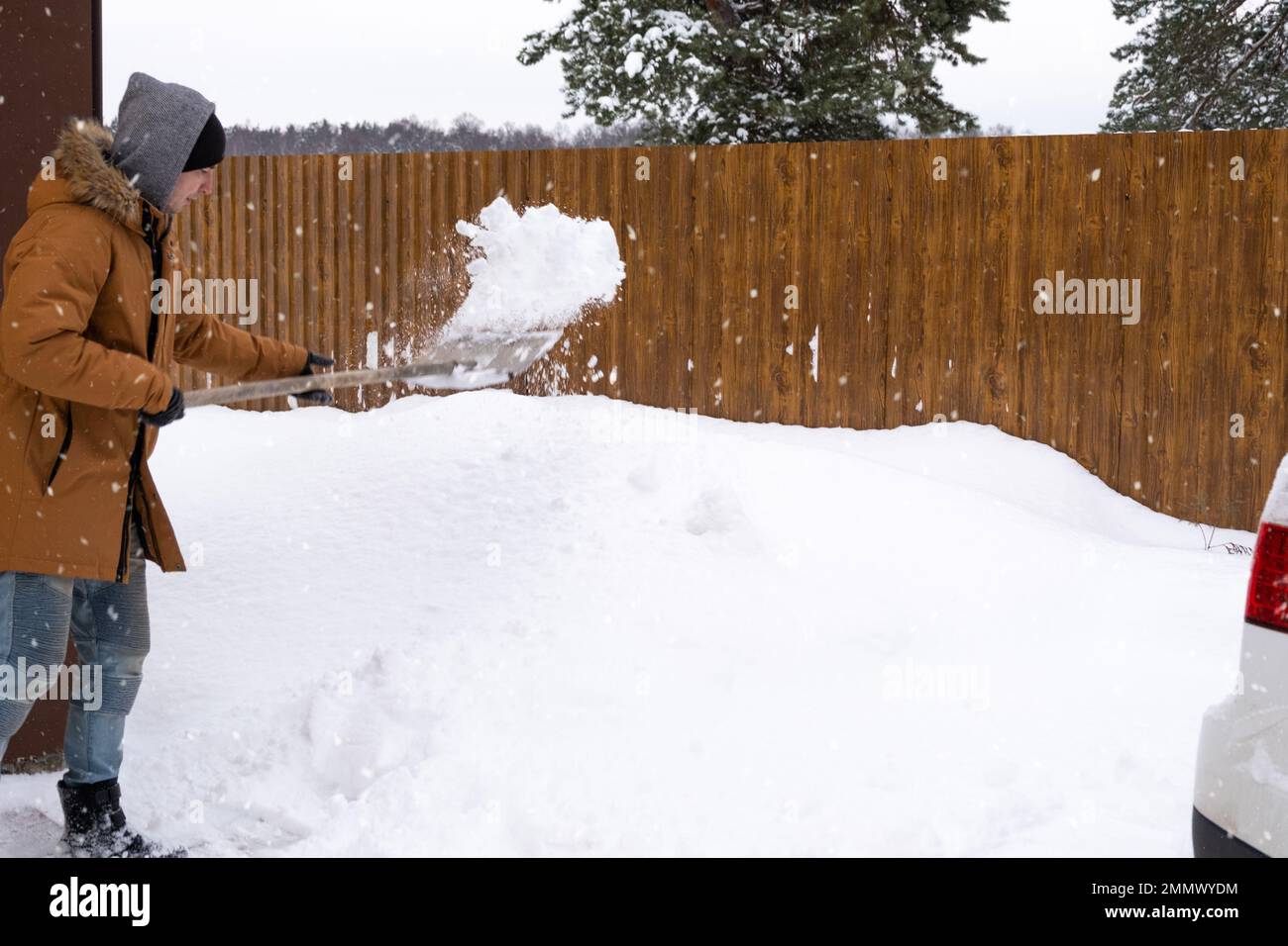A man in winter cleans snow with a shovel in the yard of a house in the