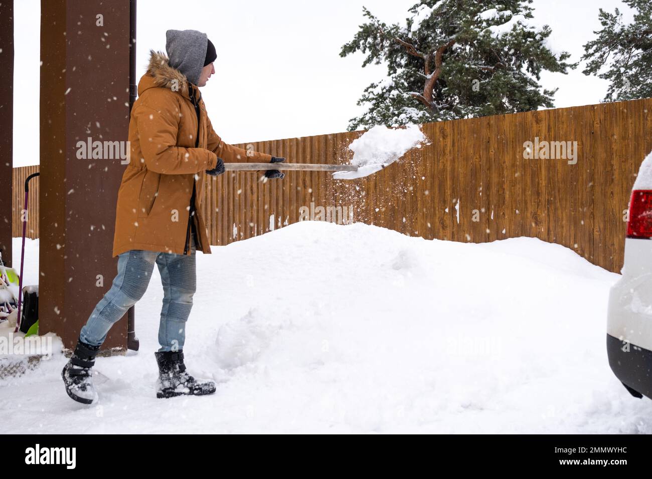 A man in winter cleans snow with a shovel in the yard of a house in the