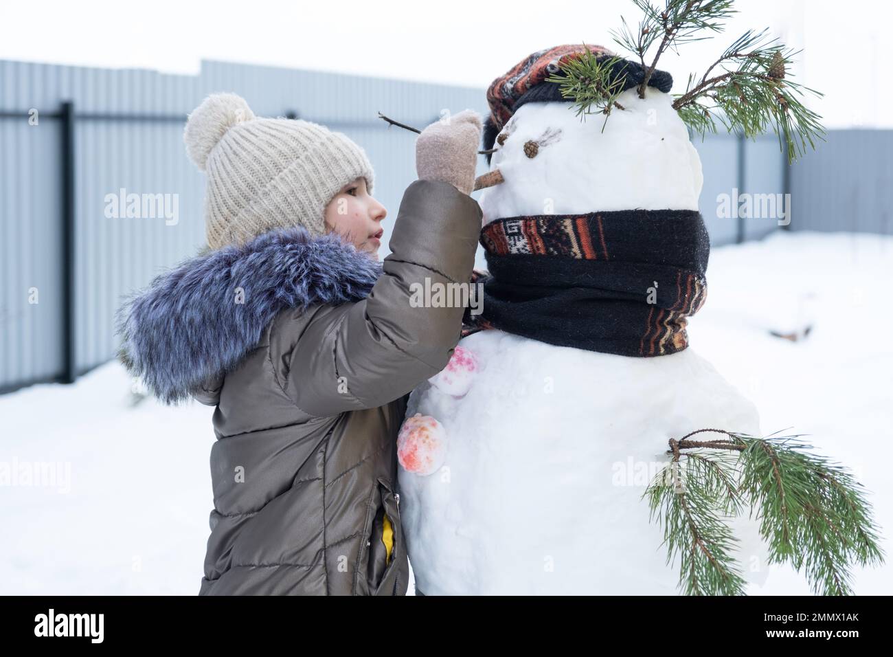 A child paints a snowman's face with paints - winter entertainment and creativity, sculpting a snowman in winter outdoor. Stock Photo