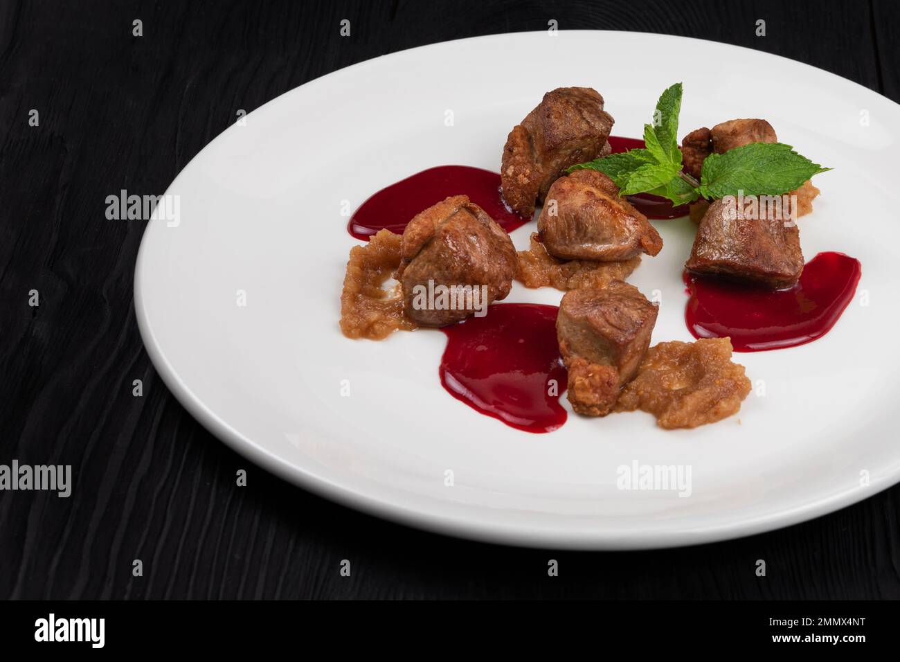 Pork meat with berries sauce and mint on white plate on wooden black background Stock Photo