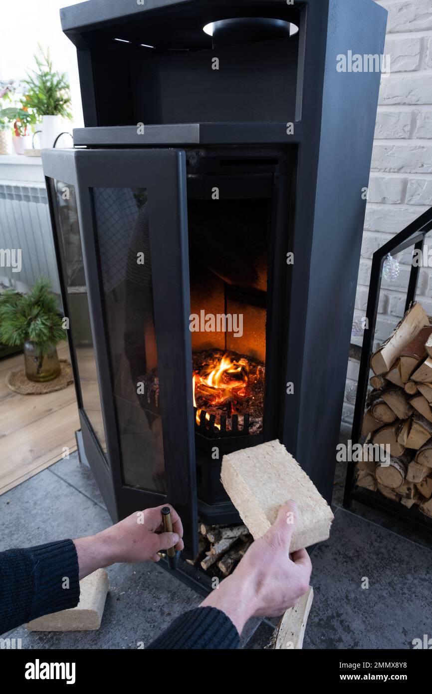 Hands kindle the hearth with economical briquettes. Fuel briquettes made of pressed sawdust for kindling the furnace - economical alternative eco-frie Stock Photo