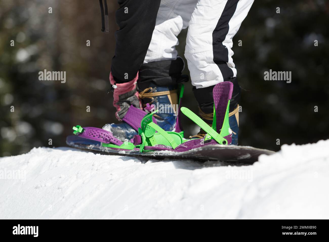 Snowboarder tying snow board deck to his feet on a slope in winter park