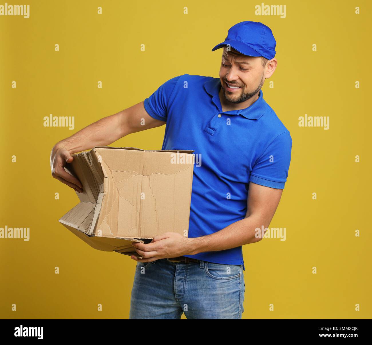 Emotional courier with damaged cardboard box on yellow background. Poor