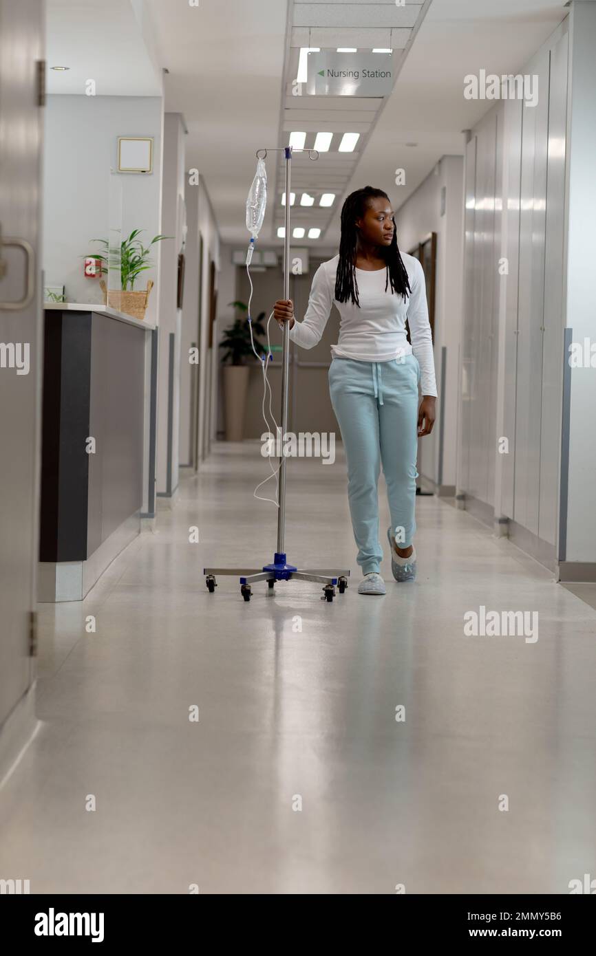 African american female patient walking through corridor with drip at