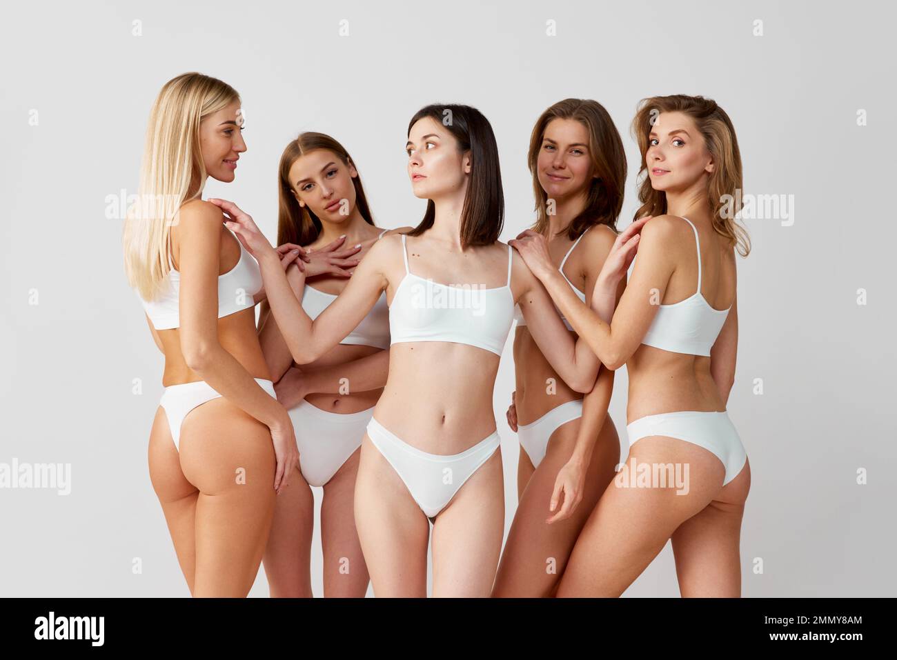Support of friends. Protection of women. Group portrait of beautiful young women posing in underwear over grey studio background. Concept of natural Stock Photo