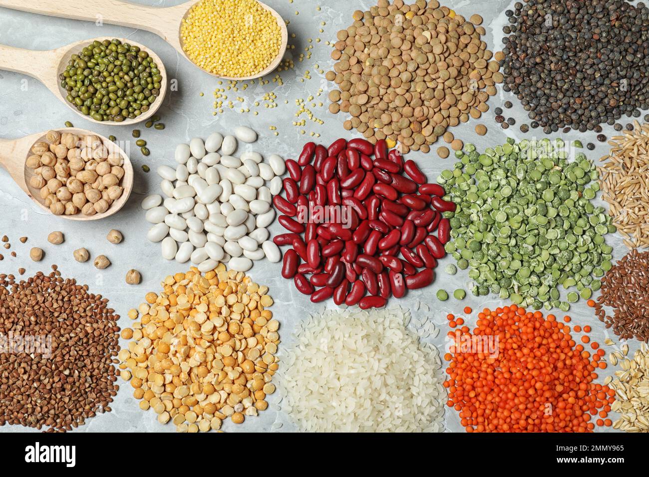 Different types of legumes and cereals on grey marble table, flat lay